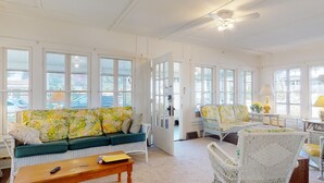 Un espai de sala d'estar ampli i ben il·luminat, amb sofàs i cadires, finestres grans i un ventilador de sostre.
