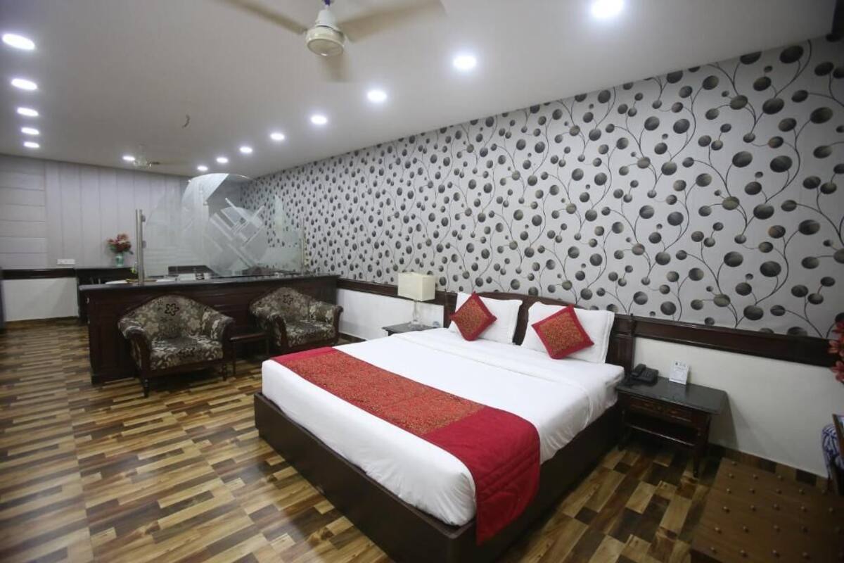 Une chambre d’hôtel avec un grand lit, un bureau, deux fauteuils et un mur décoré d’un motif.
