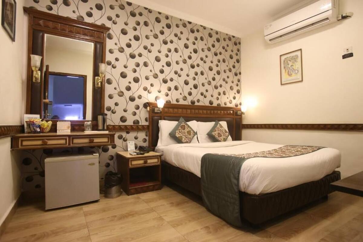 Une chambre avec un lit, une commode, un miroir, un petit réfrigérateur et un mur décoré d’un motif.