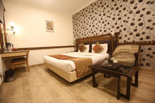A hotel room with a bed, a desk, a chair, and a small table.