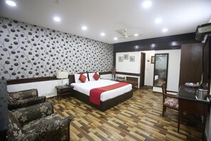 A hotel room with a large bed, a wooden floor, a patterned wall, and a desk with a chair.