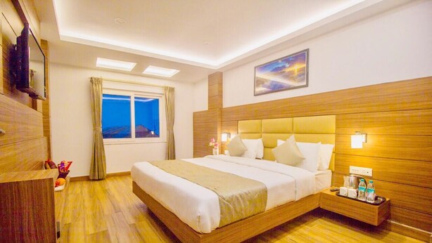 Une chambre d’hôtel avec un grand lit, une tête de lit en bois, une table de chevet avec une lampe et une fenêtre avec des rideaux.