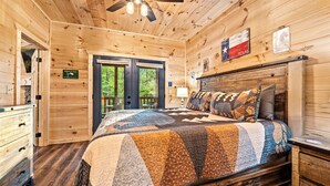 A wooden cabin bedroom with a bed, a dresser, and a ceiling fan. - Moonrise Ridge Cabin in Sevierville – Sleeps 12 • Views • Hot Tub • Game Loft (Sevierville)