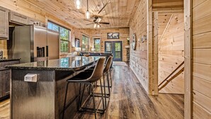 A wooden interior with a kitchen area featuring a large island, bar stools, and a refrigerator. - Moonrise Ridge Cabin in Sevierville – Sleeps 12 • Views • Hot Tub • Game Loft (Sevierville)