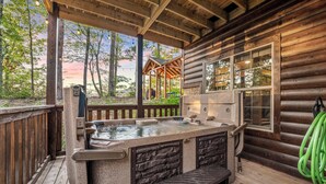 A wooden cabin with a hot tub, stone benches, and a deck overlooking a forest. - Moonrise Ridge Cabin in Sevierville – Sleeps 12 • Views • Hot Tub • Game Loft (Sevierville)