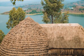 A thatched-roof structure with a view of a lake and hills in the background.