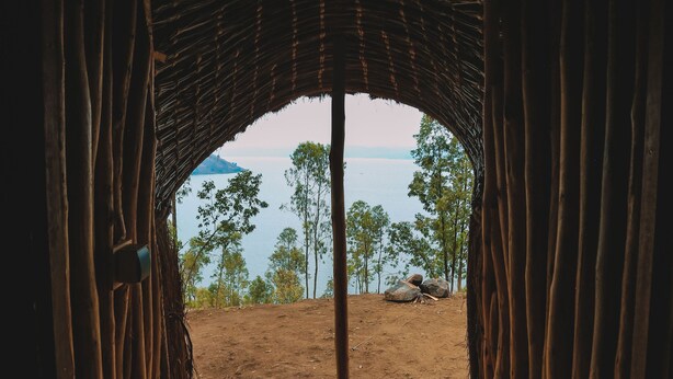 Ein rundbogiges Portal, das zu einem Ziegelweg mit Blick auf ein Gewässer und Bäume führt.