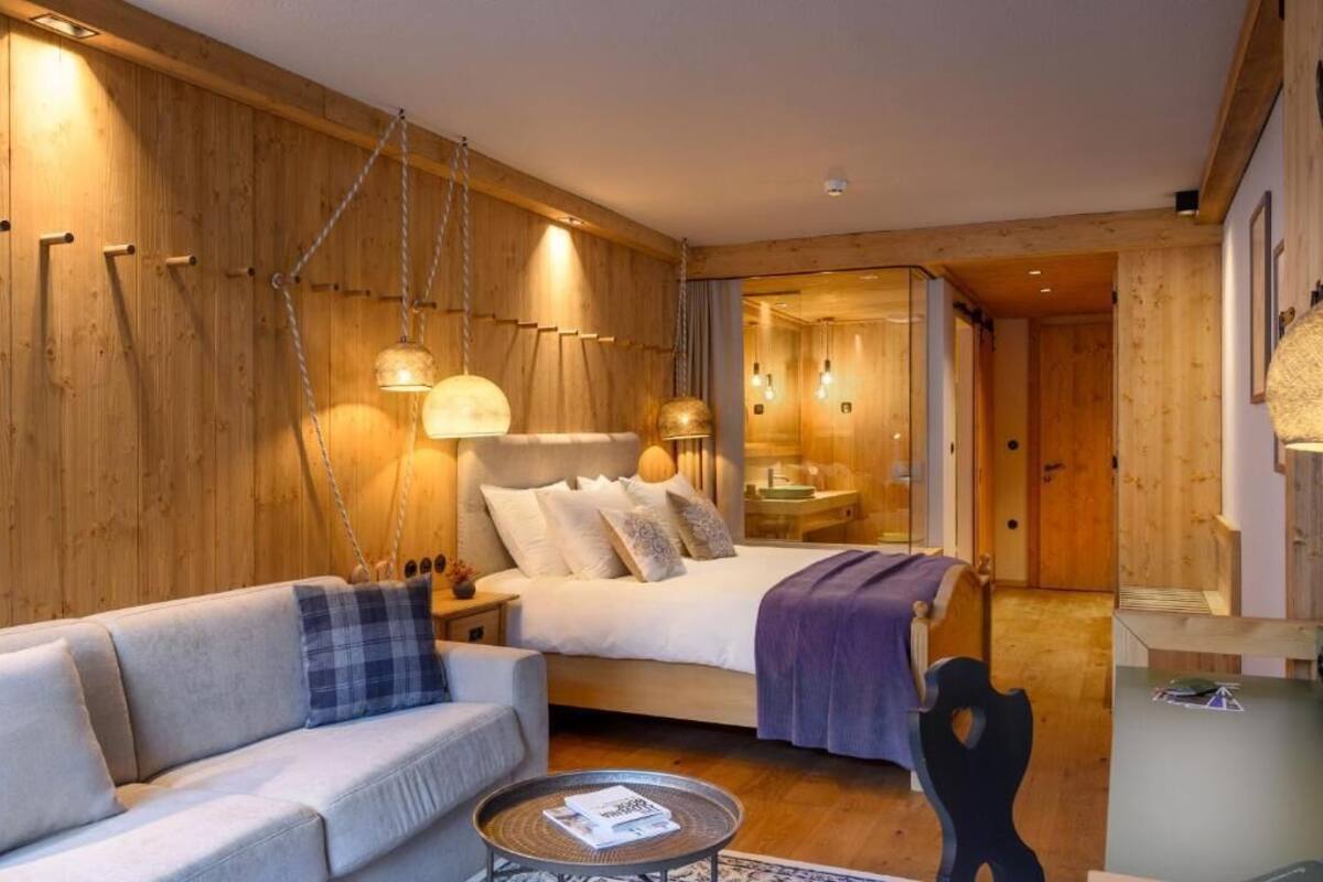 A modern bedroom with a wooden wall, a bed, a sofa, and a small table.