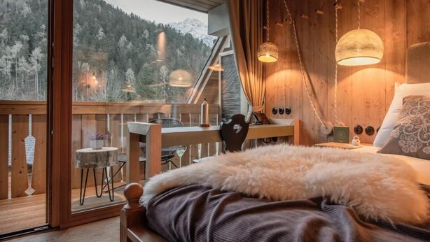 A bedroom with a large window, wooden furniture, and a view of a forested mountain. - Boutique Hotel Vila Planinka (Jezersko)