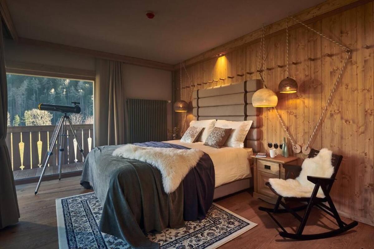 A bedroom with a large bed, a telescope, a rocking chair, and a wooden wall.