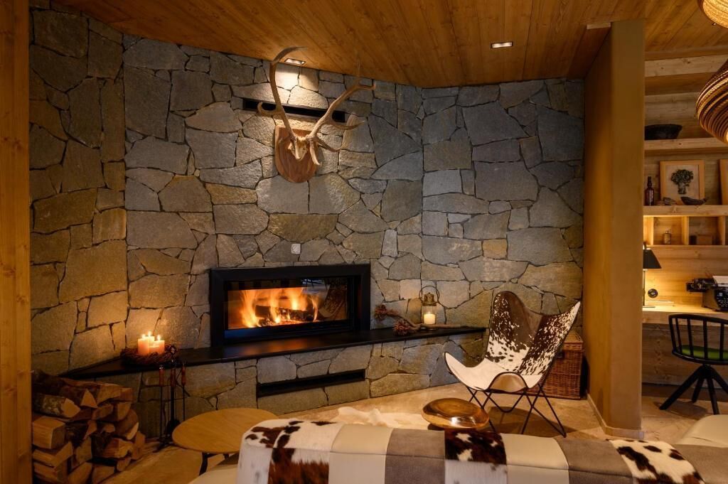 A cozy room with a stone wall, a fireplace, a cowhide-patterned sofa, and a unique chair.