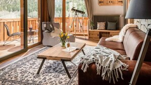 A cozy living room with a wooden floor, a sofa, a coffee table, and a telescope. - Boutique Hotel Vila Planinka (Jezersko)