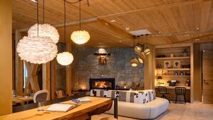A cozy living room with a stone fireplace, wooden ceiling, and a dining area with a wooden table and chairs. - Boutique Hotel Vila Planinka (Jezersko)