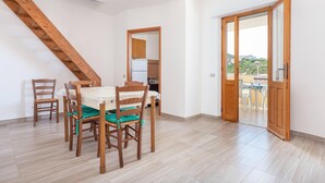 Un comedor con mesa y sillas, una escalera de madera y vistas a través de un umbral abierto.