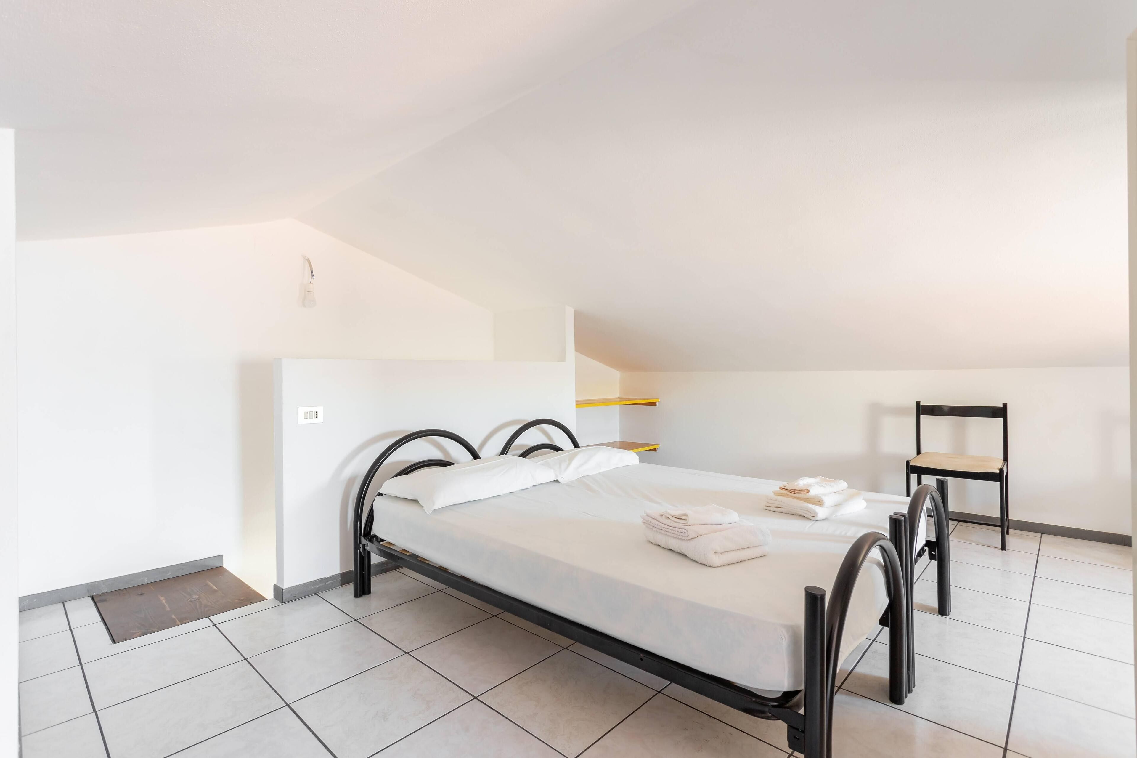 A single bed with a black frame, white bedding, and a small chair.