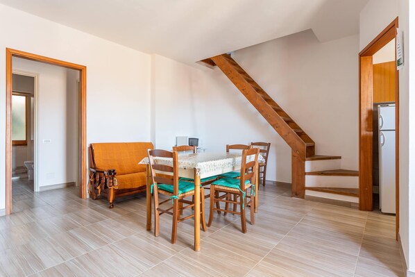 A dining area with a wooden table and chairs, a sofa, and a staircase.