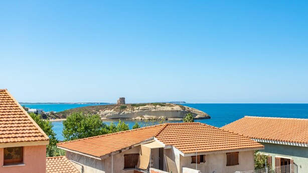Un pueblo costero con edificios de tejados de terracota, un cielo azul despejado y una vista distante del mar.