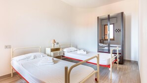 Habitación de hotel con dos camas individuales, una mesita de noche con lámpara, un armario y un espejo.