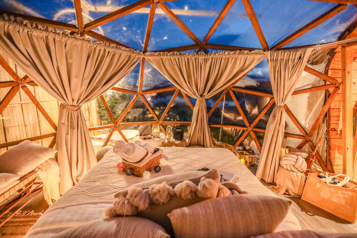 A cozy, well-lit room with a bed, pillows, and a small table with items.