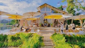 Un complexe hôtelier doté d’un espace extérieur avec des tables à parasol, d’une piscine et d’une végétation luxuriante.