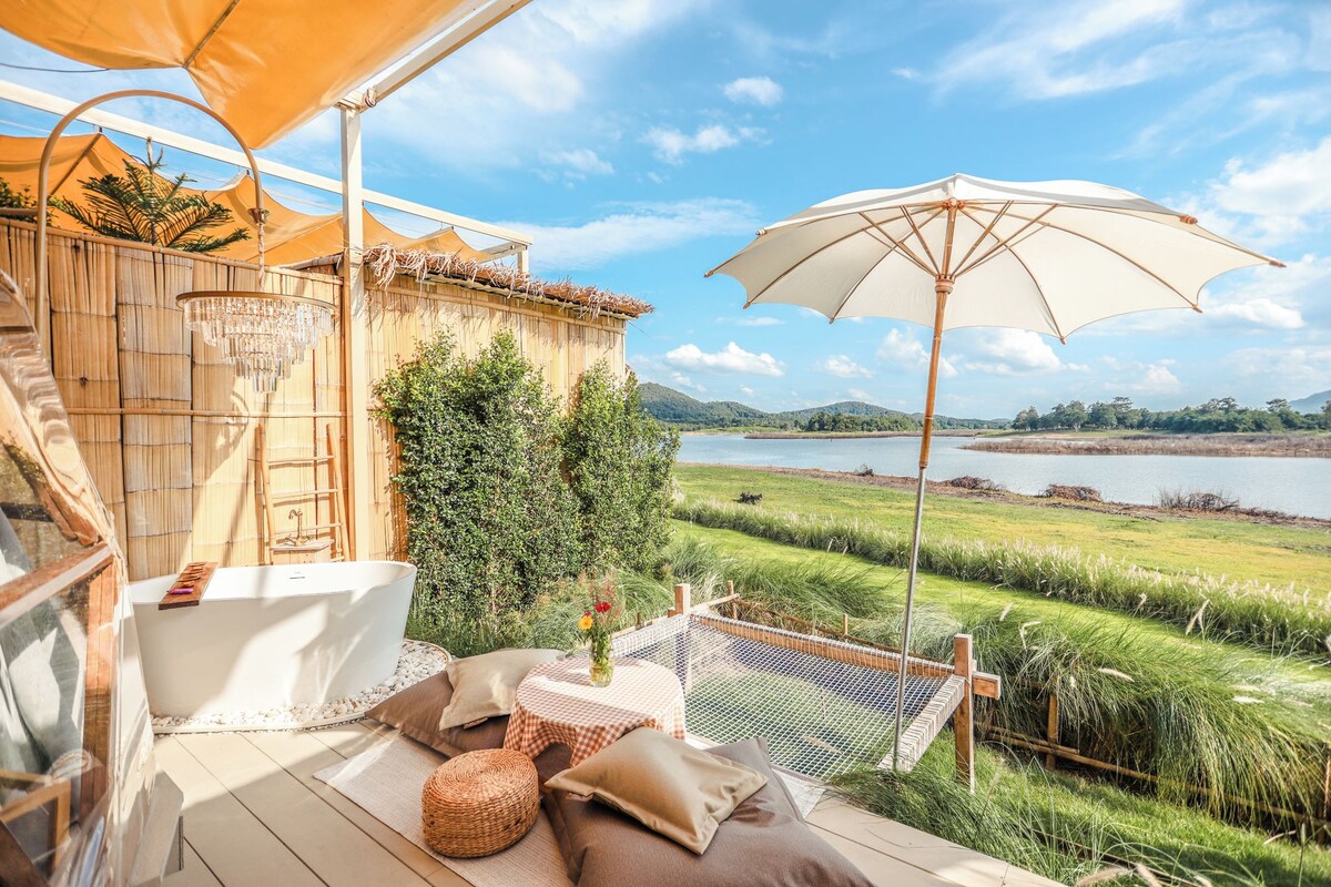 A serene outdoor seating area with a view of a lake, a bamboo fence, and a white bathtub.
