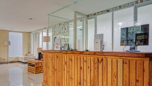 A reception desk with a wooden finish, a glass partition, and a large window. - Collection O 91288 Chrysant Premiere Residence (Malang)