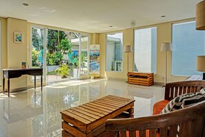 A spacious room with a piano, a wooden bench, a sofa, and a view of a pool through glass doors. - Collection O 91288 Chrysant Premiere Residence (Malang)