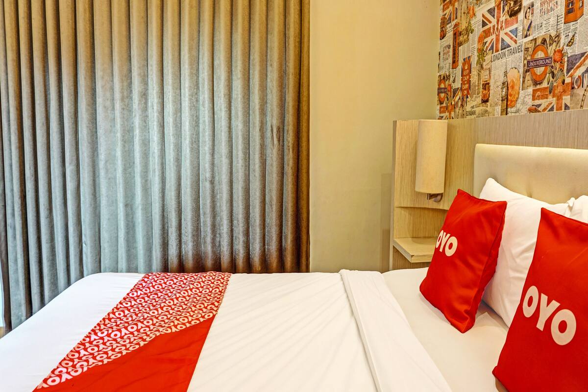 A hotel room with a bed, red and white bedding, a headboard, and a wall with a London-themed mural.