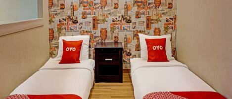 A hotel room with two beds, each with a red and white blanket and pillows with the word "OYO". The wall is decorated with a travel-themed wallpaper featuring London landmarks.