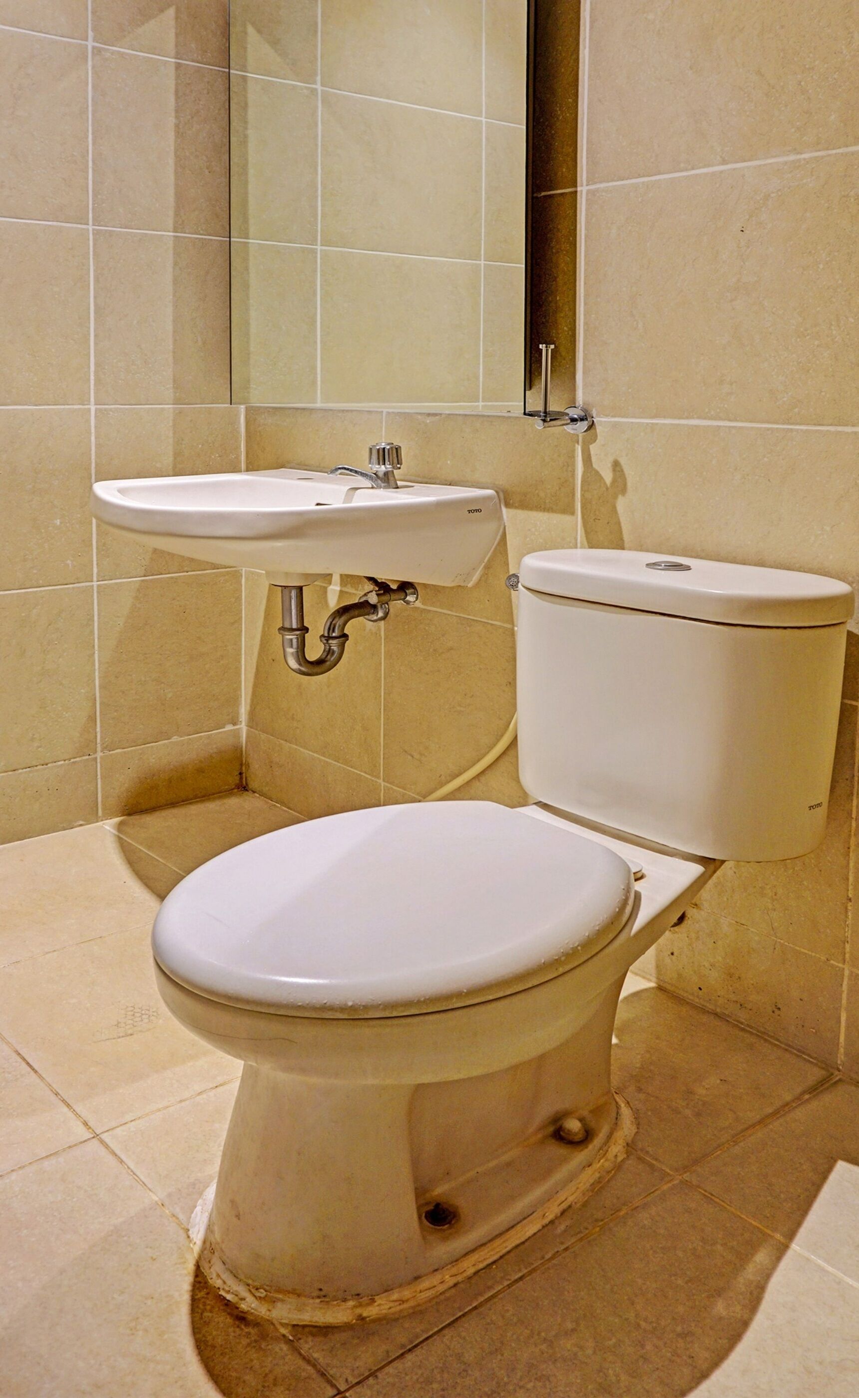 A bathroom with a white toilet, a white sink, and beige tiled walls.