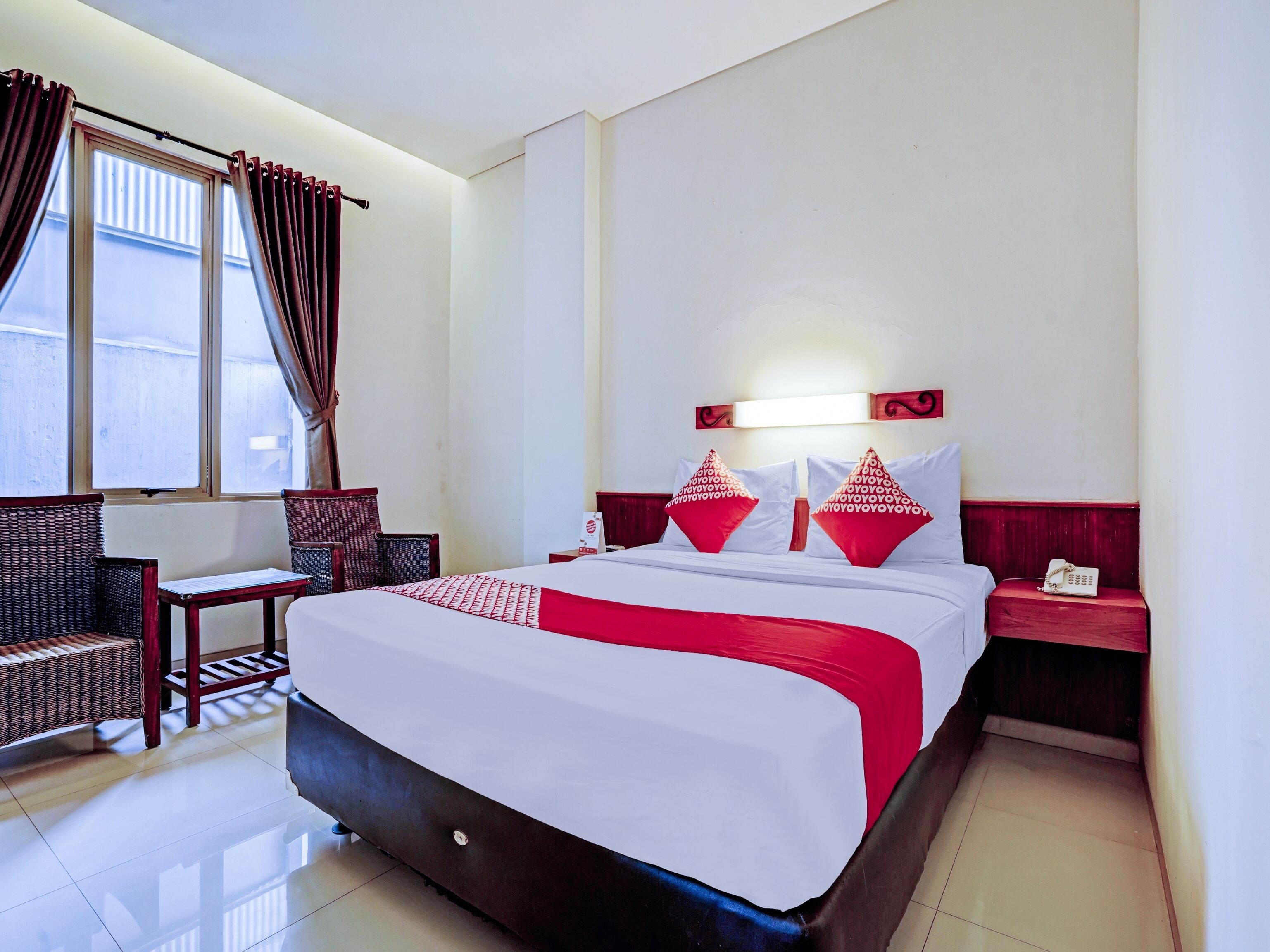 Habitación de hotel con una cama grande, dos mesitas de noche, una butaca y una ventana con cortinas.