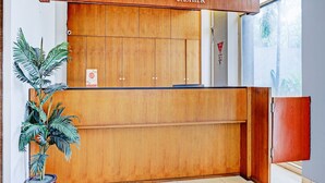 A reception desk with a wooden finish, a sign indicating 'RECEPTION' and 'CASHIER', and a potted plant to the left. - Collection O Riau Near Trans Studio Bandung Formerly Hotel Montameri (Bandung)