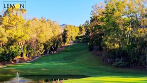 Ein Golfplatz mit einem Wasserelement, umgeben von Bäumen und einem Zaun.