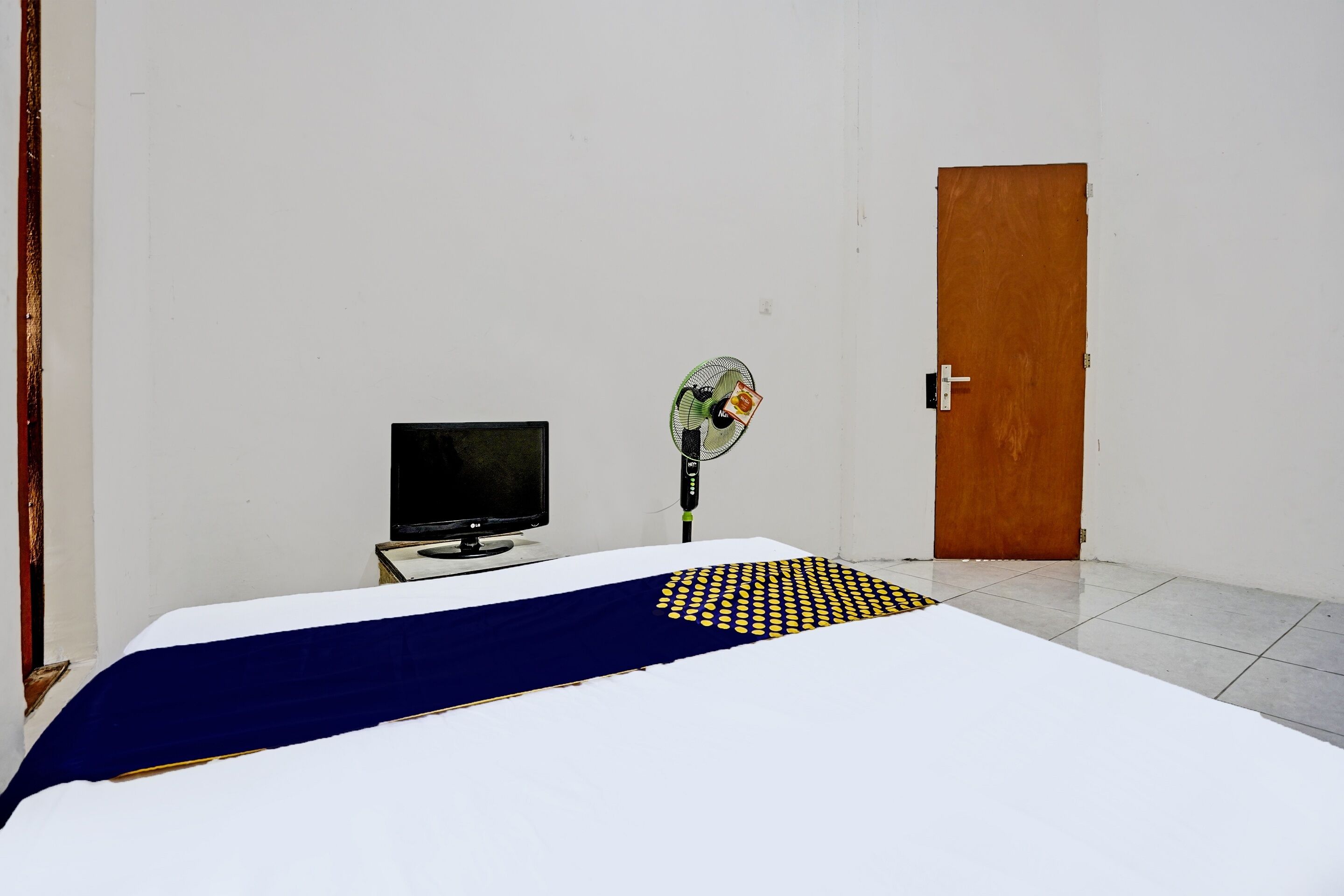 A room with a bed, a television, a fan, and a door.