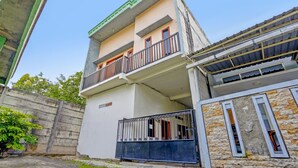 Een meerlaags gebouw met een balkon op de tweede verdieping, een hekwerk aan de ingang en een gevel van natuursteen.