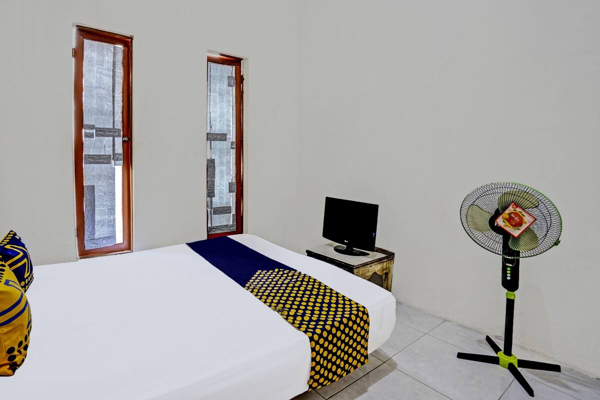 Ein Zimmer mit einem Bett, einem Fernseher auf einem kleinen Tisch und einem Standventilator.