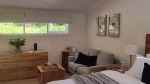Une chambre à coucher comprenant un lit, une commode, un canapé, une fenêtre et des œuvres d’art encadrées accrochées au mur.