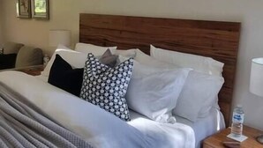 Un lit bien fait, avec une tête de lit en bois, des oreillers blancs à motifs et un plaid gris.