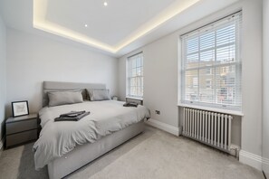 A bedroom with a large bed, a nightstand, a radiator, and a window with blinds. - City Centre - Townhouse - Stay 10 - Cinema Room (London)