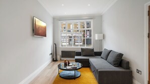 A modern living room with a grey sofa, a round coffee table, and a large window with a view of buildings. - City Centre - Townhouse - Stay 10 - Cinema Room (London)