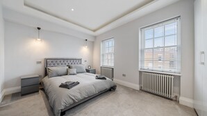 A bedroom with a large bed, two bedside tables, a radiator, and a window with blinds. - City Centre - Townhouse - Stay 10 - Cinema Room (London)