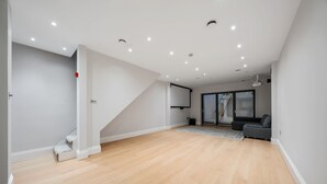 A spacious living area with a wooden floor, a staircase, a grey sofa, and a large window. - City Centre - Townhouse - Stay 10 - Cinema Room (London)