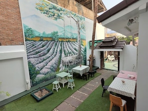 A courtyard with a mural of a field and trees, outdoor seating, and a small shrine. - Kaysorn Residence  (Chiang Mai)