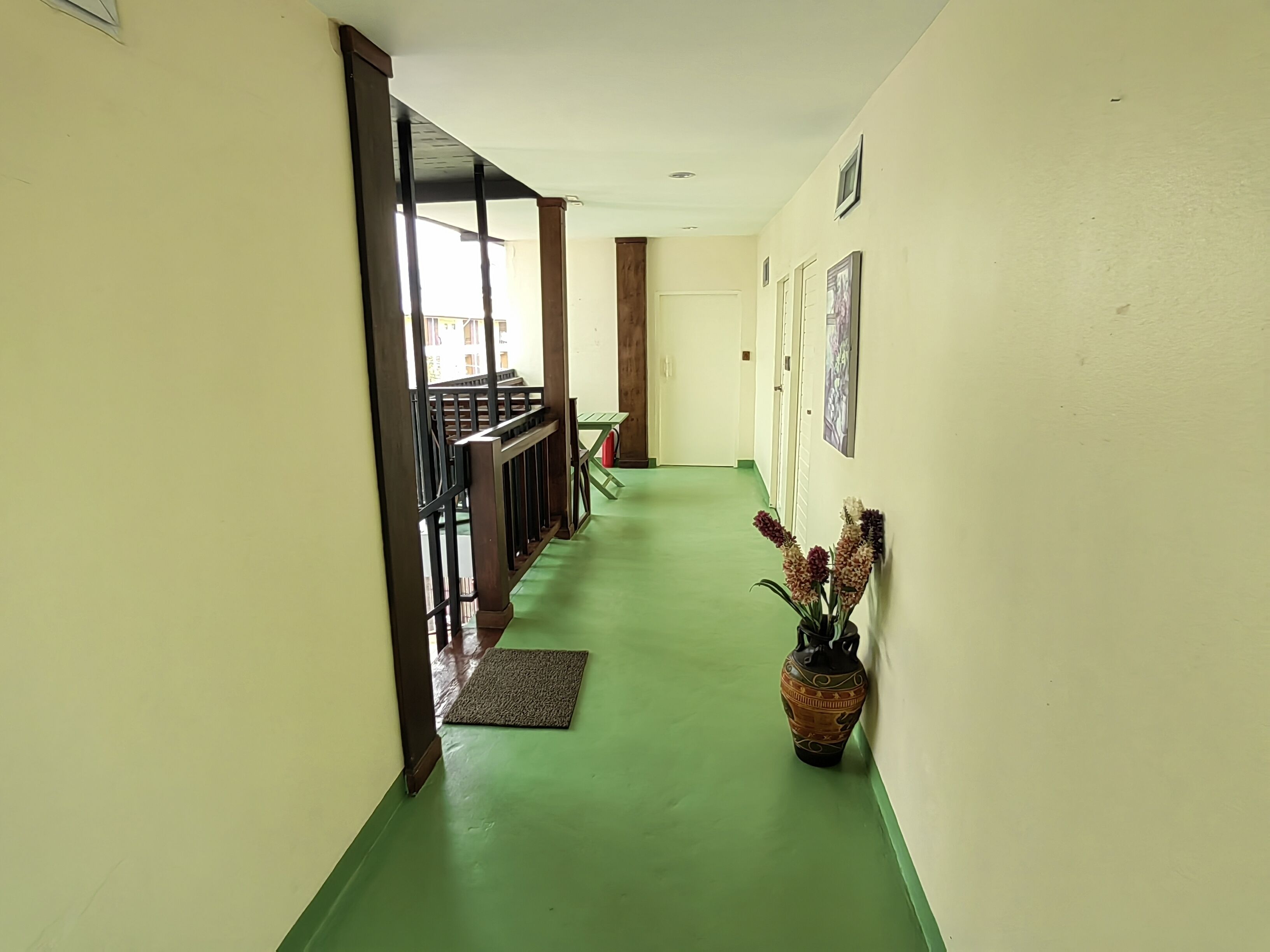 Corredor com piso verde, corrimãos de madeira e uma porta que dá para outro quarto.