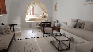 Una sala de estar con un sofá, una silla de madera, una mesa de centro de vidrio y una cama con dosel.