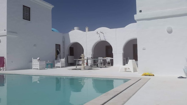 Un área de piscina con paredes blancas, arcos y mobiliario para exteriores.