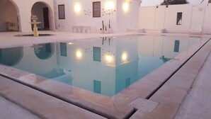 Una piscina con superficie de agua cristalina, rodeada por un edificio blanco con arcos en puertas y ventanas.