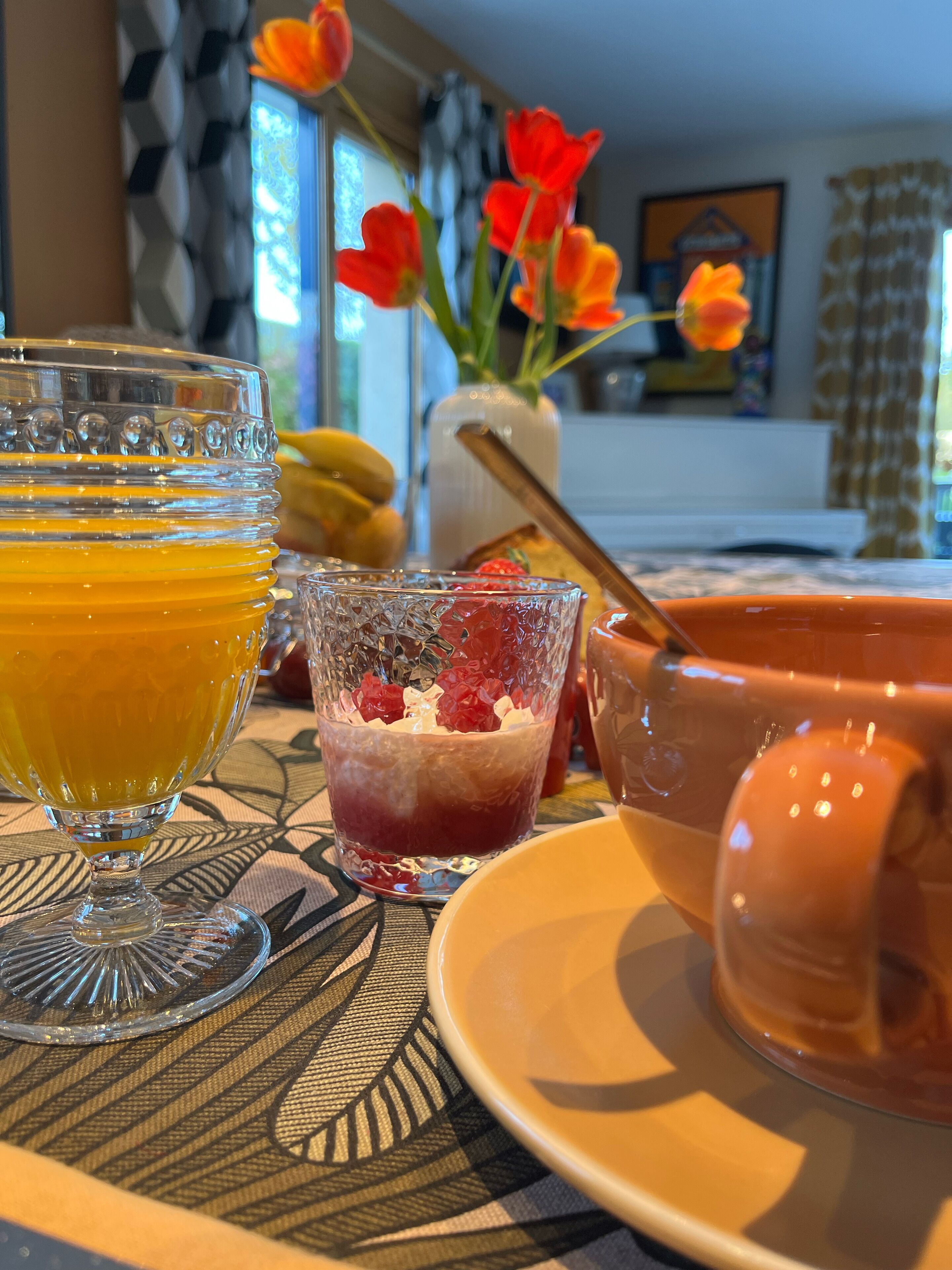 Une table avec un verre de jus d’orange, un verre de fruits rouges mélangés et un bol de soupe.