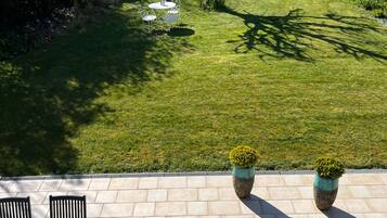 A patio with a round table and chairs, two potted plants, and a view of a well-maintained lawn and trees.