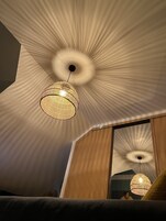 Um interior moderno com design de teto único, uma luminária pendente de vime e um espelho grande que reflete o ambiente.